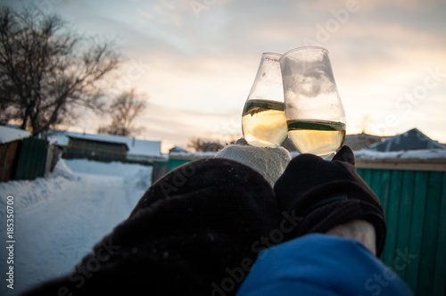 Male and female hands with glasses of white wine on a sunset background in winter