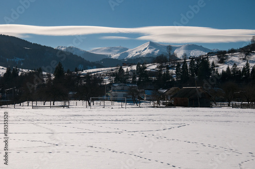 Mountain village in the background of the winter Carpathians. Traces of animals on a winter field, covered with snow against the backdrop of mountain peaks.