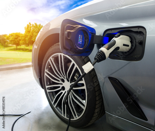 EV Car or Electric car at charging station with the power cable supply plugged in on blurred nature with sun light background. Eco-friendly alternative energy concept photo