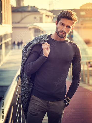 One handsome young man in urban setting in European city, standing, smiling and looking at camera
