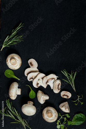 Top view of fresh mushrooms with mash salad and rosemary on a black stoned surface