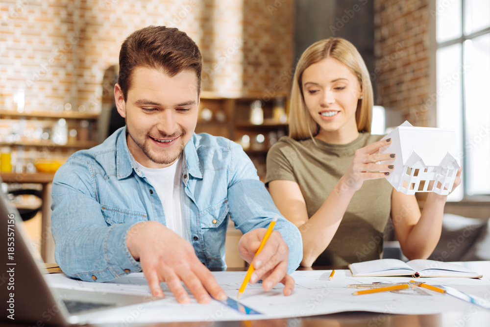 Own building. Two cute amazing male and female colleagues planning house while looking down and sitting at the table Own building. Two cute amazing male and female colleagues planning house while looking down and sitting at the table