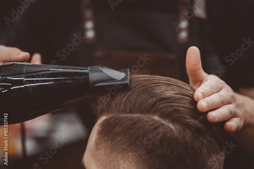 Close-up, master Barber does the hairstyle and styling with hair dryer, dries hair to guy. Concept Barbershop. Soft focus.