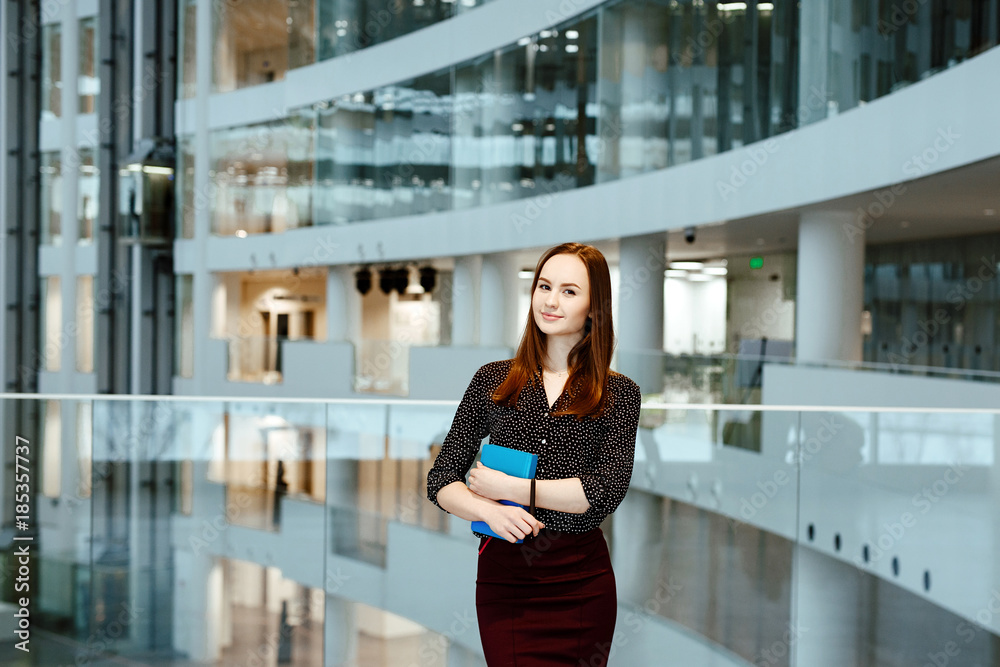 The young business woman with the daily log in hands against the background of office.