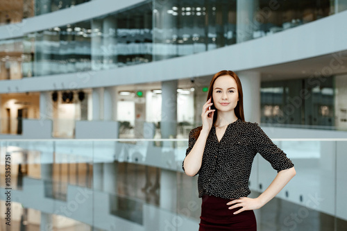 The young business woman talks on the smartphone against the background of office.