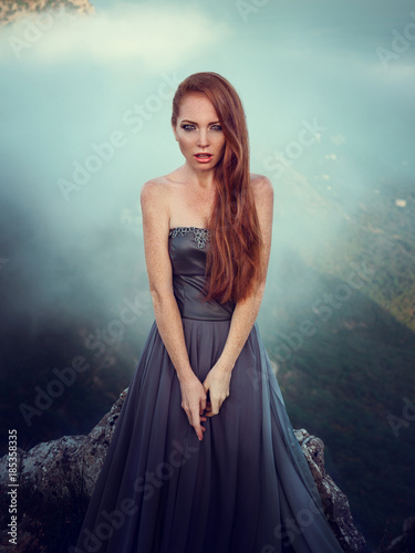 Summer outdoors portrait of beautiful furious scandinavian warrior ginger woman in grey dress with metal chain mail.