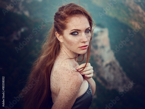 Summer outdoors portrait of beautiful furious scandinavian warrior ginger woman in grey dress with metal chain mail.