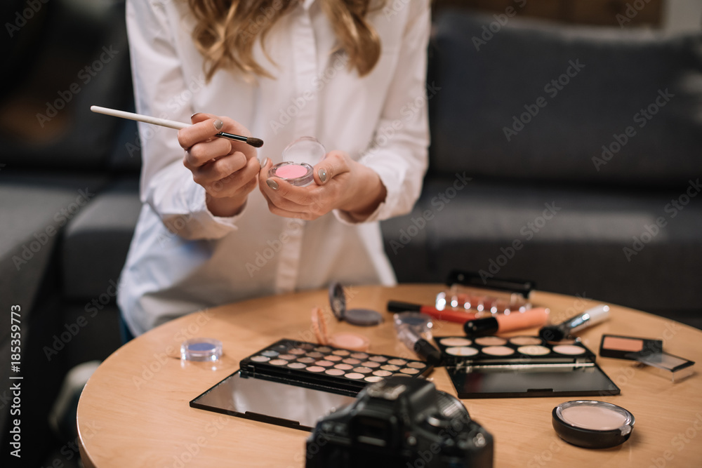 cropped image of beauty blogger holding makeup brush and eyeshadow in hands