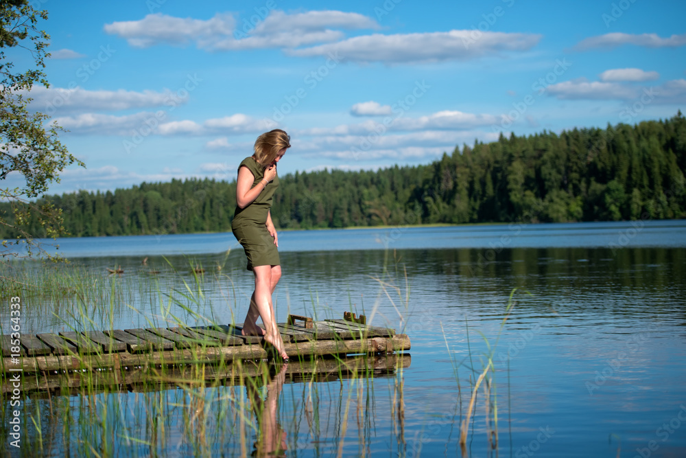 Beautiful girl touches the water standing on a wooden jetty at a lake