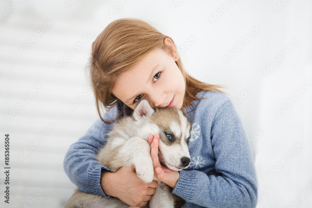 Happy Little girl lying on a bed and hugging with the puppy husky dog