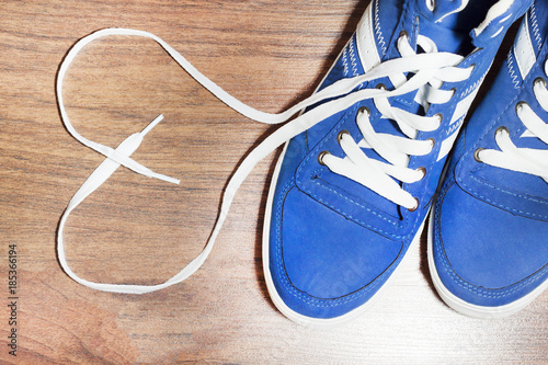 White Leather Shoes with Untied Laces in Heart Form on Wooden Floor