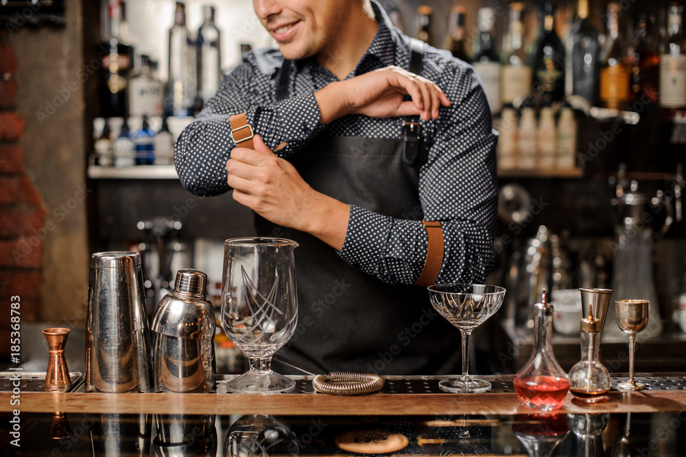 Smiling barman standing behind the bar counter with a bar equipment
