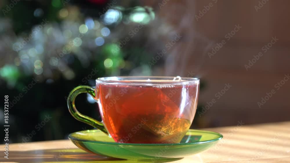 Steaming cup of hot black tea with a Christmas tree on the background Steaming cup of hot black tea with a Christmas tree on the background