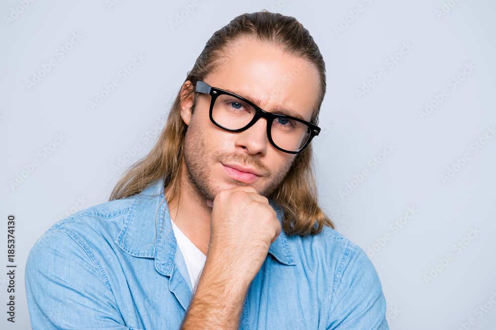 Close up portrait of attractive, clever, stunning man in jeans shirt and glasses holding arm on chin, looking at camera thoughtful expression over grey background Close up portrait of attractive, clever, stunning man in jeans shirt and glasses holding arm on chin, looking at camera thoughtful expression over grey background