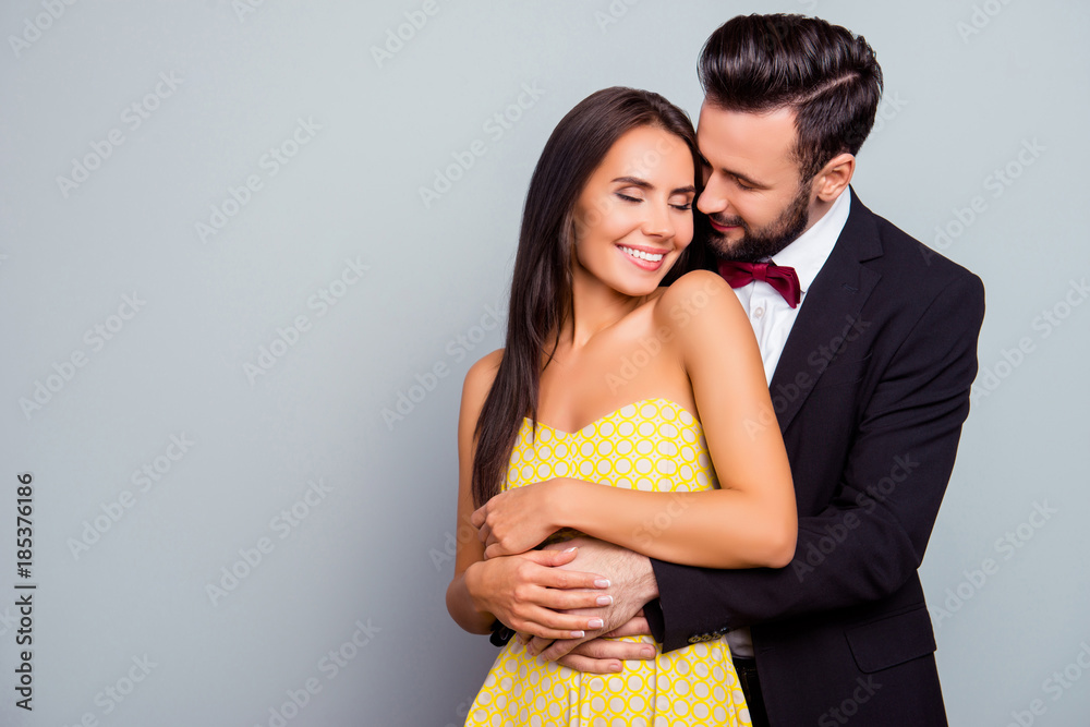 Photo  of beautiful, cheerful, positive, cute, sensual, tender couple  enjoying hugs with each other having eyes close over grey background  with copy space, gentle husband's hands touch his wife - obrazy, fototapety, plakaty 