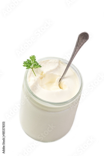 close up of sour cream pot with spoon and parsley in on white background top view