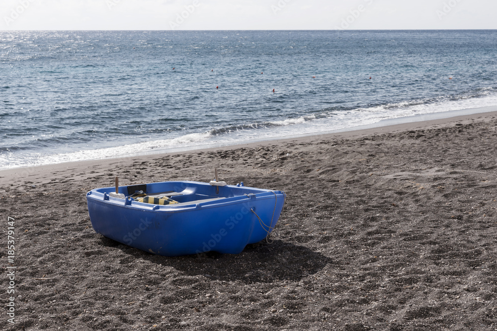 Blue plastic boat on black sand at the beach