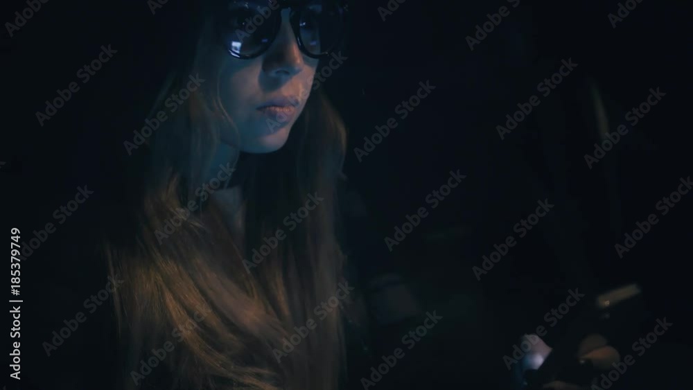 Attractive young woman in glasses uses an application on a smartphone sitting in the car at night Attractive young woman in glasses uses an application on a smartphone sitting in the car at night