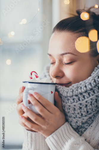Fototapeta Close up of woman drinking hot chocolate next to the window