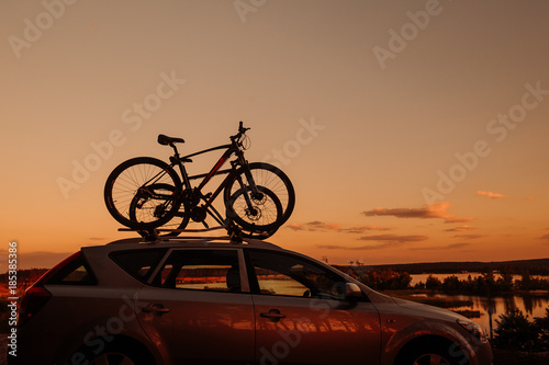 Passanger car with two bicycle mounted to the roof. Sunset.