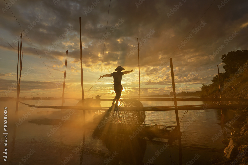 The silhouette fisherman on during mist sunrise,Thailand