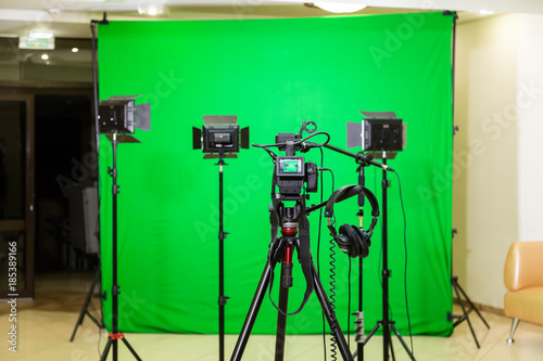 The camera on the tripod, led floodlight, headphones and a directional microphone on a green background. The chroma key. Green screen