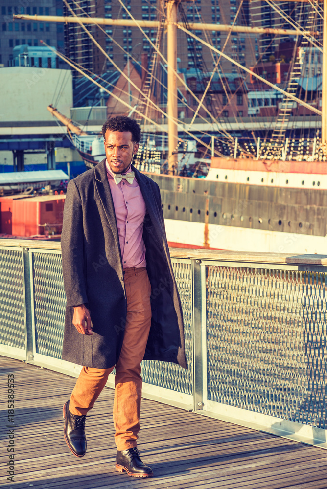 African American Businessman Traveling In New York. Wearing Woolen  Overcoat, Pink Shirt, Brown Pants, Leather Boot Shoes, Bow Tie, Black Man  With Beard, Looking Around, Walking On Harbor In Sunset. Stock Photo |