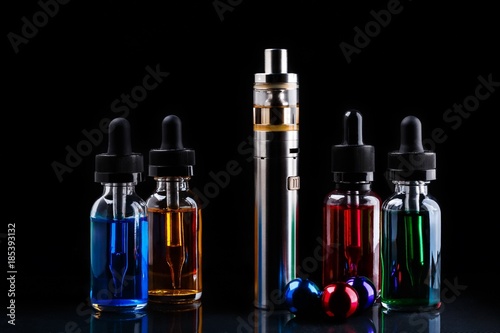 Electronic cigarette, bottles with vape liquid and small christmas balls on black background