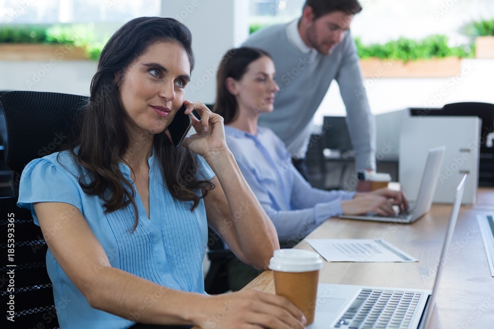 Female executive talking on phone while holding coffee mug Female executive talking on phone while holding coffee mug