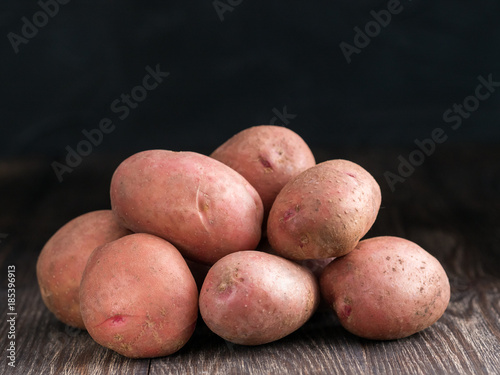 Raw whole organic potatoes on old brown wooden background. Copy space. Low key.