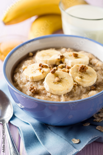 Oatmeal porridge with banana, walnuts and honey in bowl on purple wooden background. Healthy breakfast.