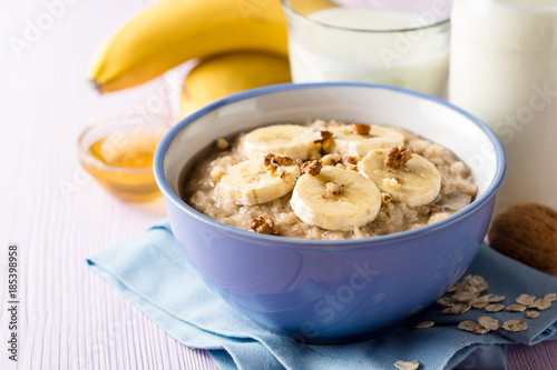 Oatmeal porridge with banana, walnuts and honey in bowl on purple wooden background. Healthy breakfast.