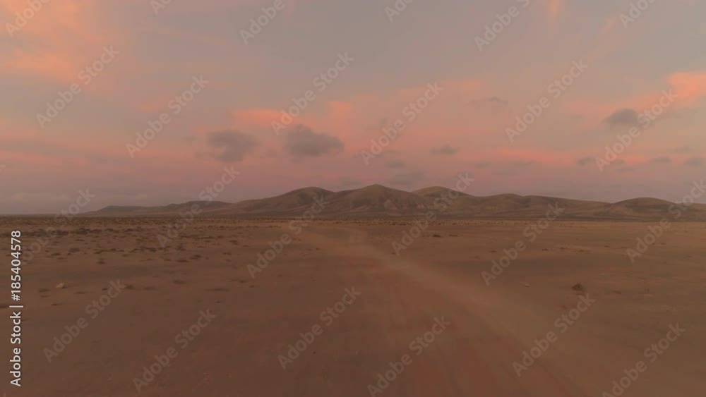 AERIAL: Flying towards a large volcanic structure in pink colored desert sunset. Barely visible dirt tracks running through empty landscape. Quiet and colorful summer sunset in lonely volcanic desert. AERIAL: Flying towards a large volcanic structure in pink colored desert sunset. Barely visible dirt tracks running through empty landscape. Quiet and colorful summer sunset in lonely volcanic desert.