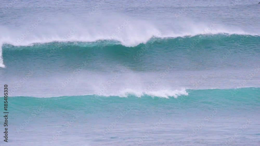 SLOW MOTION Large barrel waves closing in on the coast while surfers are lining up in the background. Pro surfers paddling against the breaking waves to reach the line-up on a cloudy summer afternoon