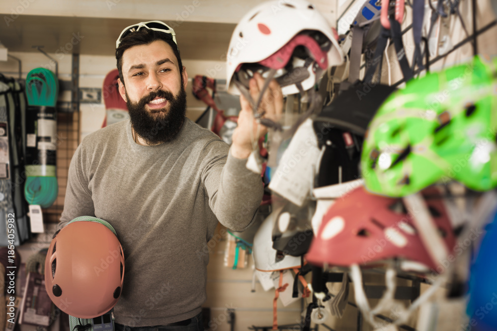 cheerful male customer examining helmets in sports equipment sto