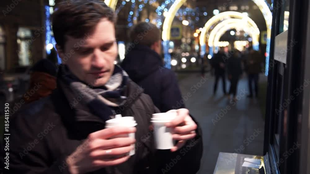 Young man buying in coffeeshop paper cup of coffee on city street at night. Young man buying in coffeeshop paper cup of coffee on city street at night.