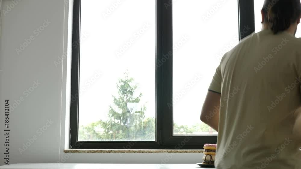 Man is taking a cup of coffee and donut from the plate next to a window Man is taking a cup of coffee and donut from the plate next to a window