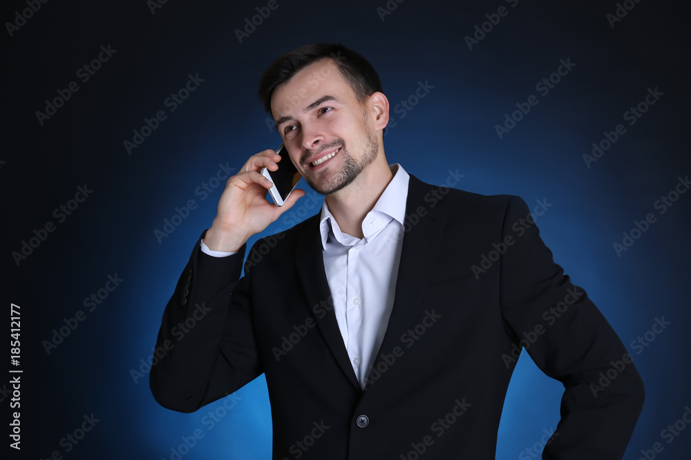 Man in formal suit talking on phone against dark background Man in formal suit talking on phone against dark background