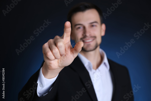 Handsome man in formal suit touching invisible screen on dark background