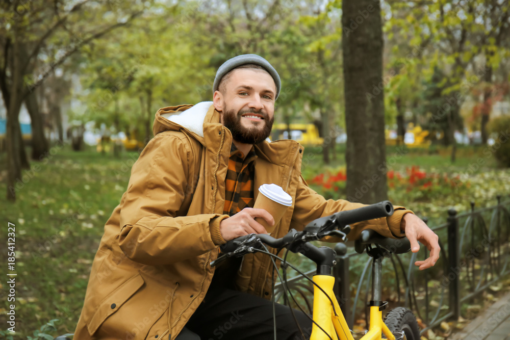 Fototapeta premium Attractive young hipster with cup of coffee and bicycle in park
