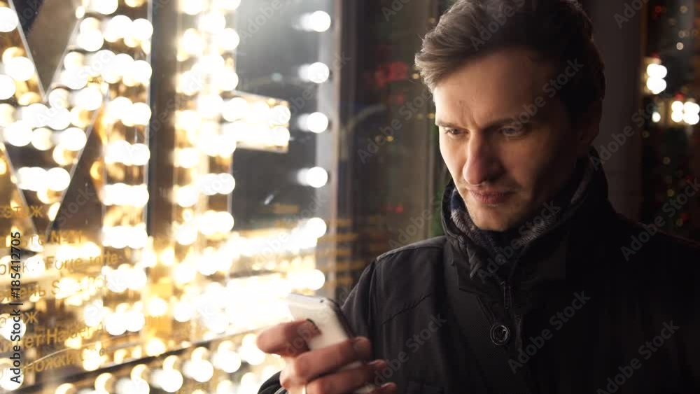 Young man using smartphone on a urban street in evening standing near storefront Young man using smartphone on a urban street in evening standing near storefront