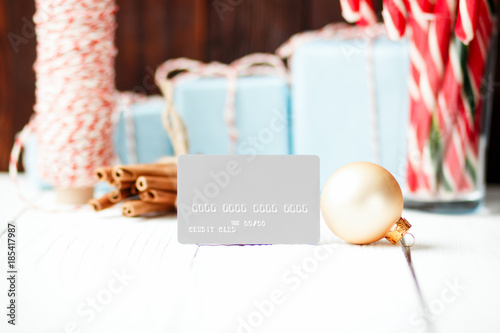 Christmas composition New Year selling discount concept gray credit card with xmas gifts sweets toys balls rope cinnamon on white wooden table and brown background