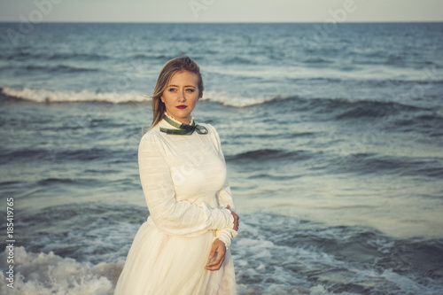 Young beautiful woman portrait, she has a white tulle dress and she is getting into the sea - Portrait of a poetic, vintage woman walking into the ocean, romantic mood