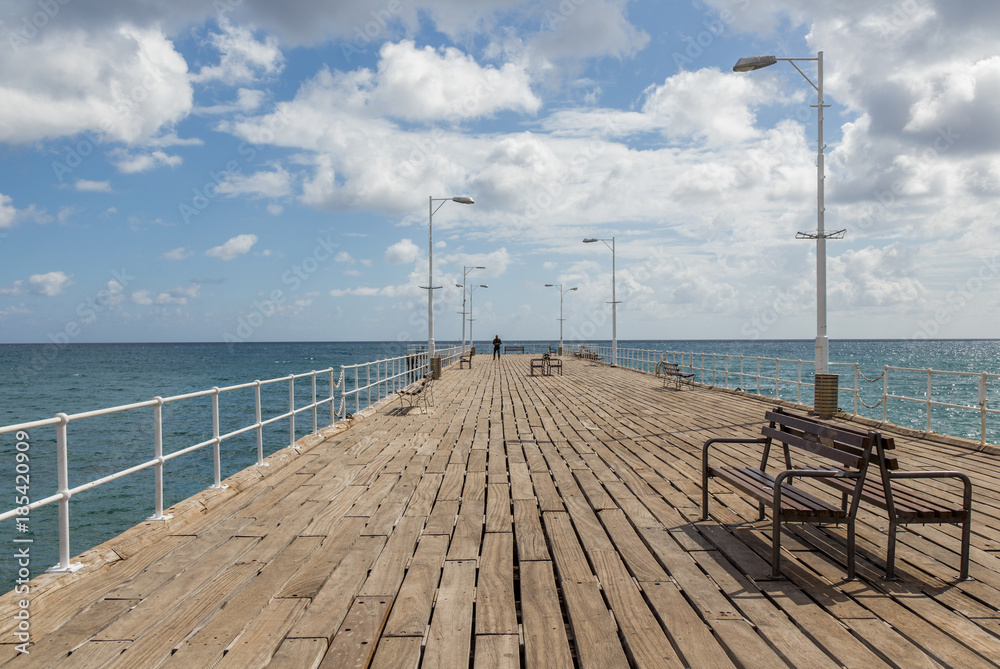 Single person at the end of long wooden  jetty with benches and lamps.