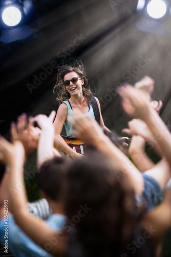 A young woman playing guitar on stage during a concert outside