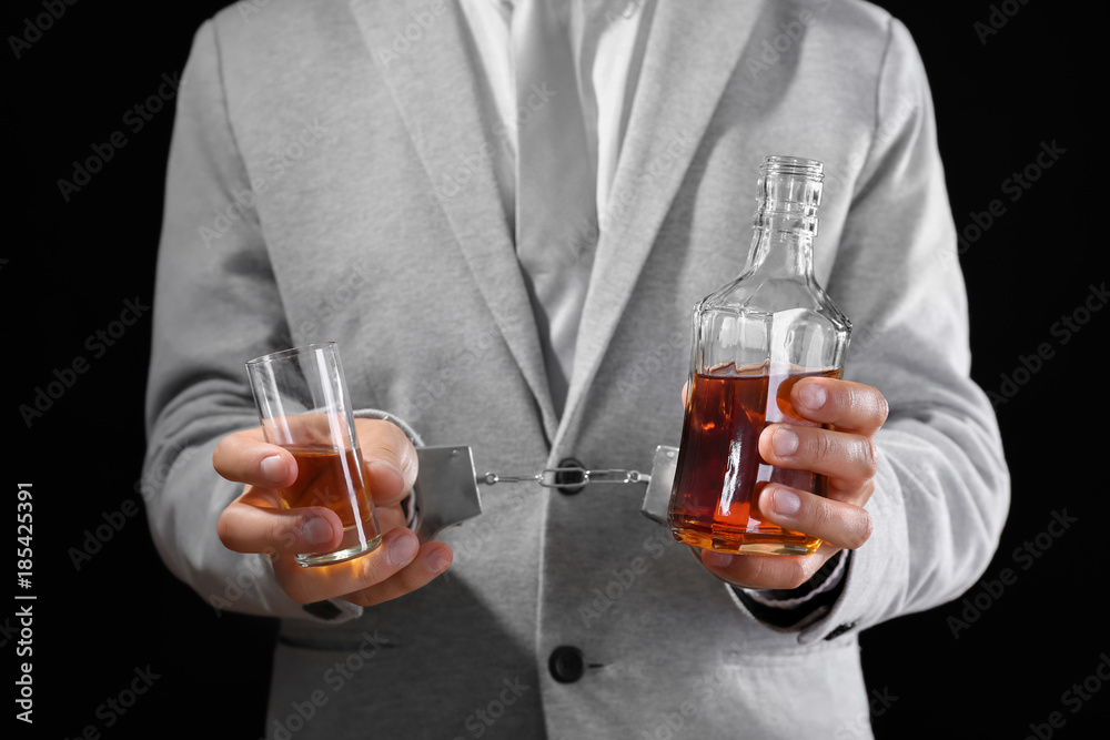 Man in handcuffs with bottle and glass of brandy on dark background. Alcohol dependence concept Man in handcuffs with bottle and glass of brandy on dark background. Alcohol dependence concept