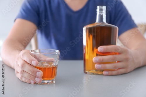 Man with glass and bottle of whiskey indoors. Alcohol dependence concept