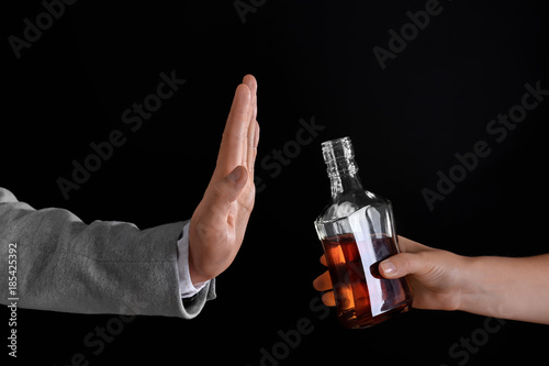 Hand of man rejecting bottle of alcohol against dark background