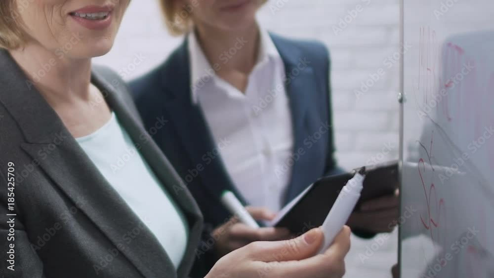 Businesswomen discussing successful project, looking at information on board Businesswomen discussing successful project, looking at information on board