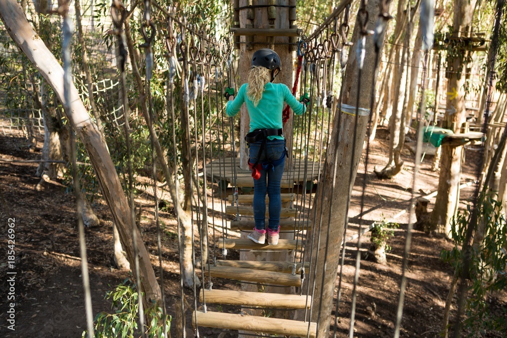 Little girl wearing helmet crossing wooden bridge in the forest Little girl wearing helmet crossing wooden bridge in the forest